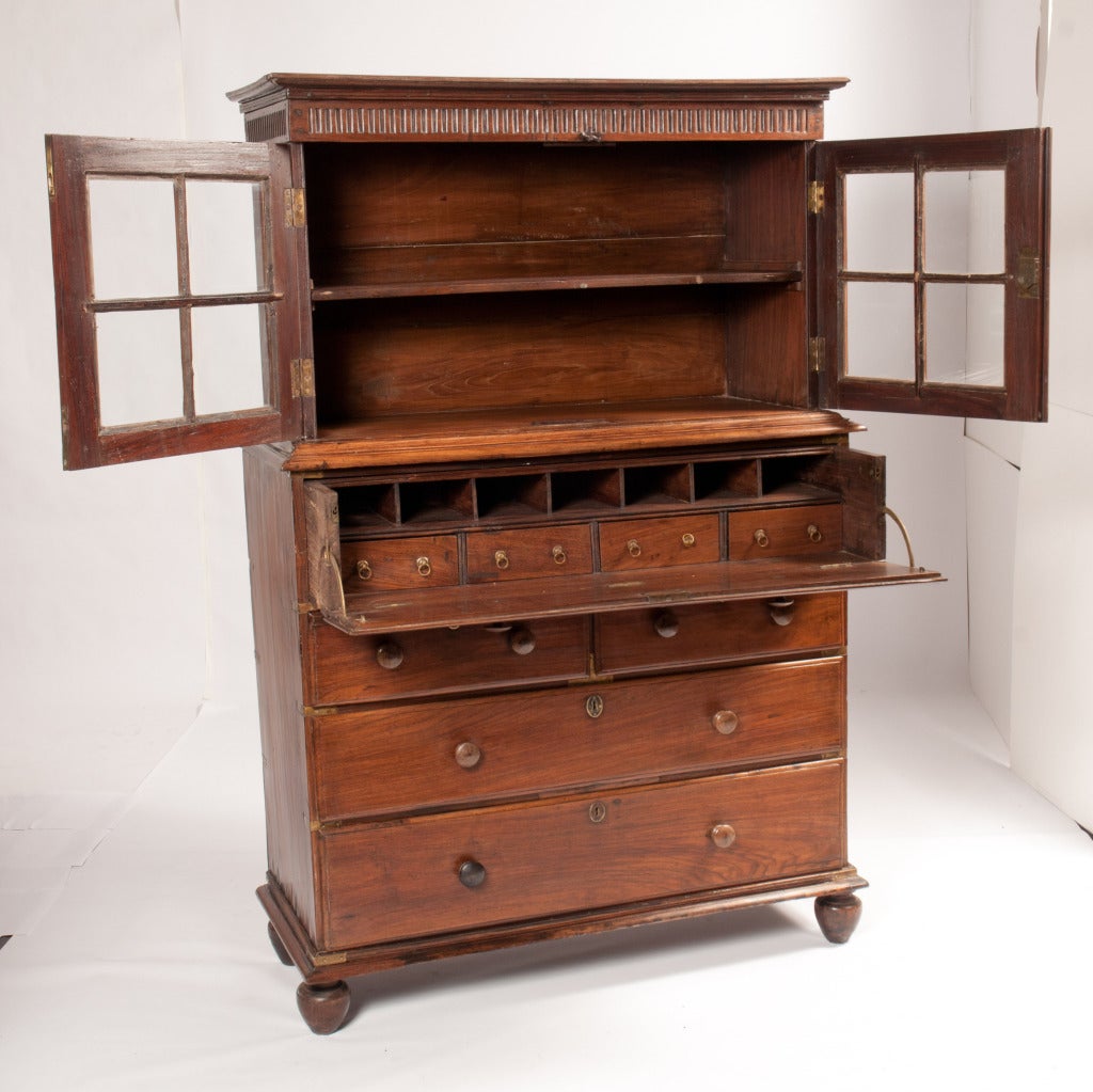 British campaign secretary consisting of a top glass panel door cabinet with single shelf. Bottom cabinet has a secretary with four drawers and seven compartments. Two drawers over two drawers, brass corner braces. Drawers have wooden knobs with