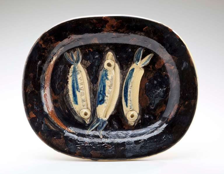 Picasso (1881-1973) glazed earthenware platter highlighted by three sardines.  Glazed in black and brown with three yellow and blue glazed sardines with defined eyes.  Signed with impressed mark on the back