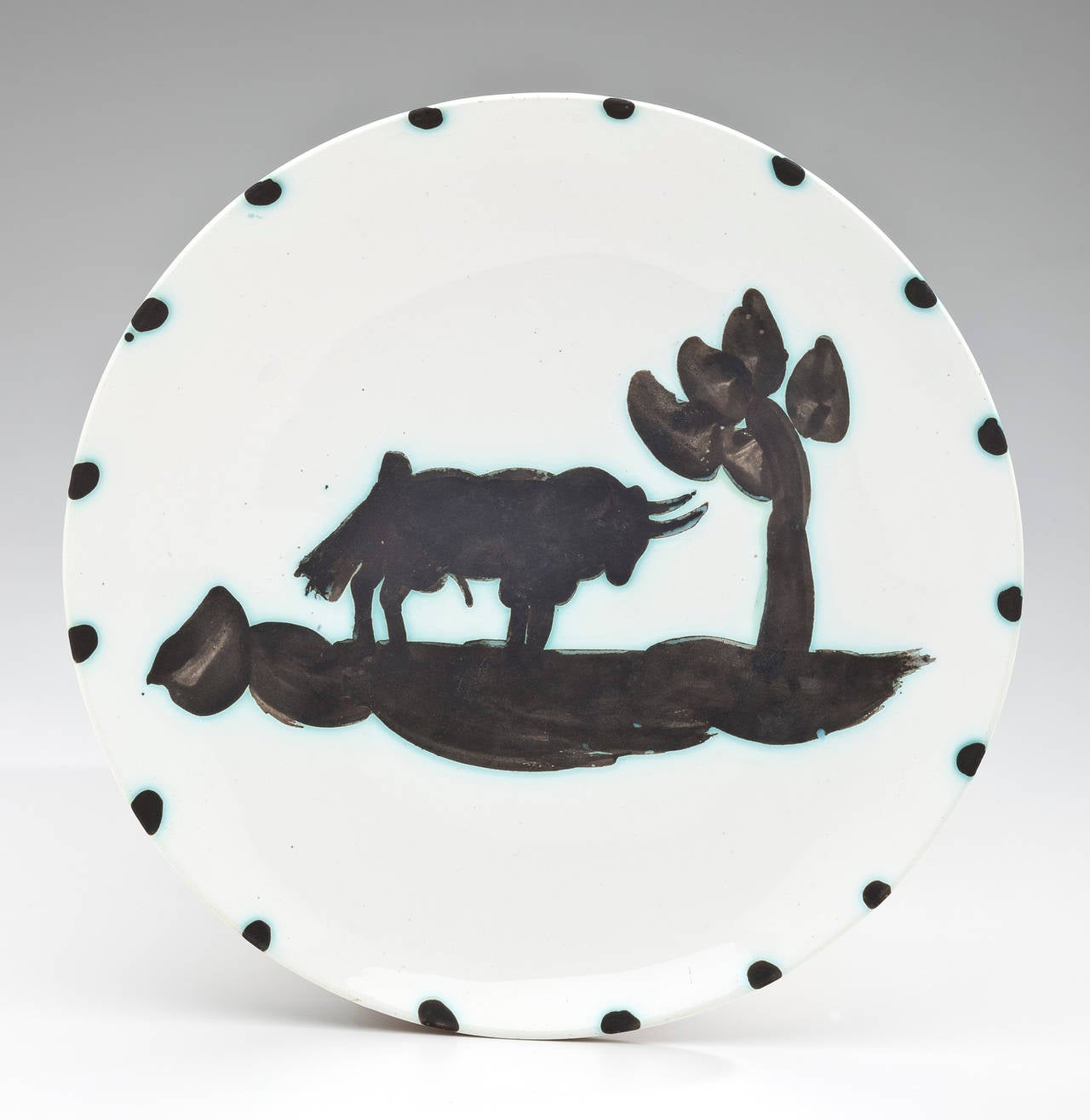 A ceramic plate by Pablo Picasso (1881-1973) showing a bull sunning himself under a tree. White earthenware clay with a white enamel decoration and green shading. Signed on the bottom 