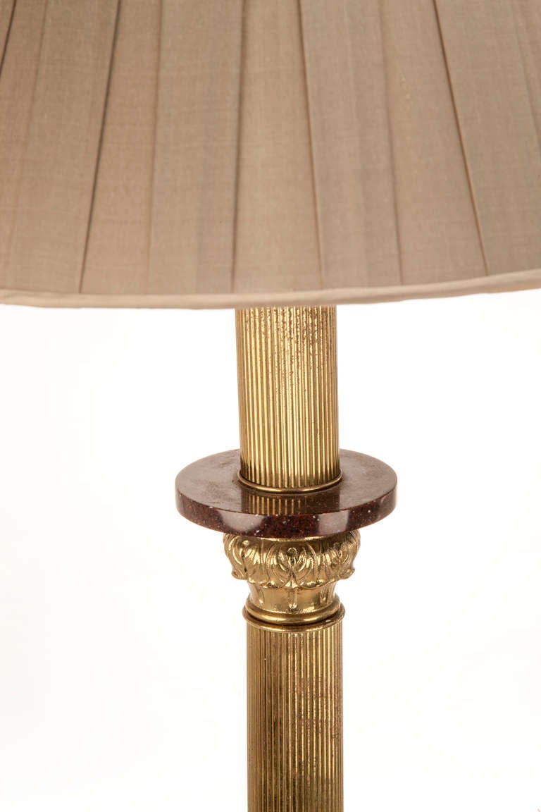 Reeded brass floor lamp with acanthus leaf details dividing the shaft, on a round base with an insert of faux porphyry, finely chased border on three paw feet, new box pleated taupe silk shade with a reeded brass finial.