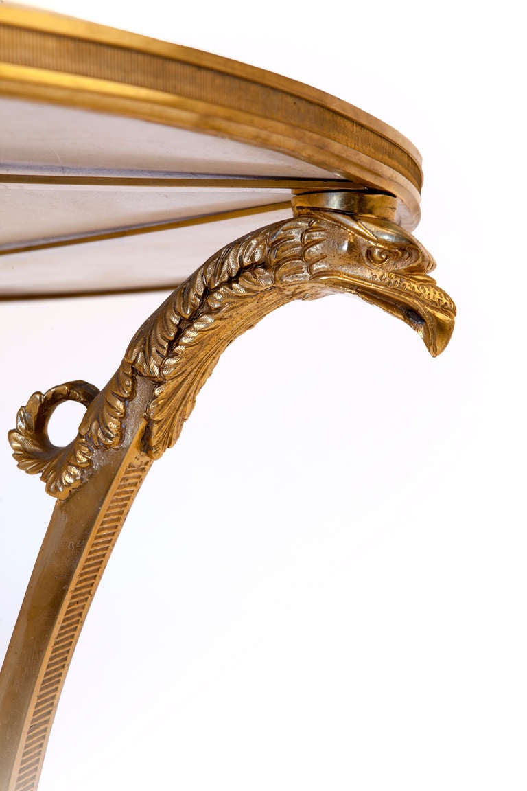 French Empire Style three legged gueridon table, upper and lower round tops of polished marble, unusual triangular stretcher beneath lower shelf, the three bronze supports having finely chased eagles' heads at top, and foliate hoof feet at bottom.