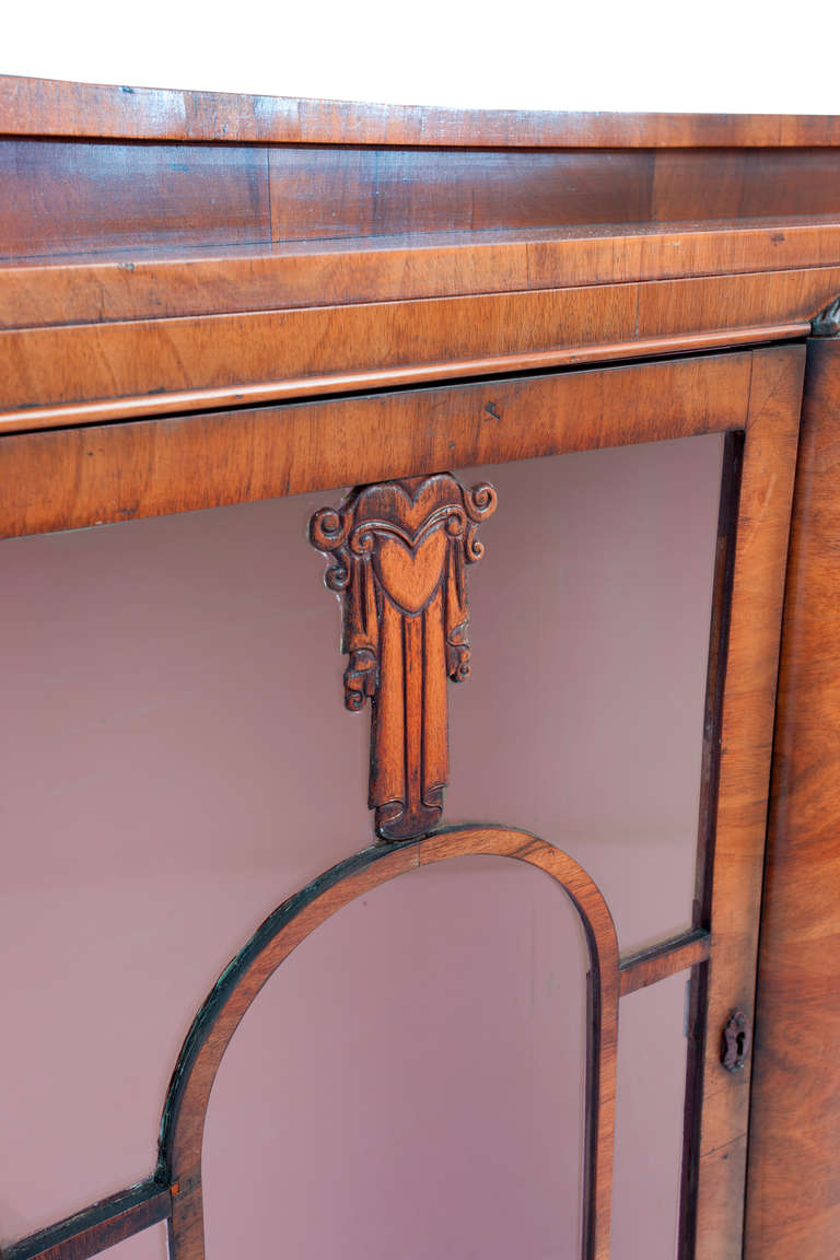 Biedermeier style Art Deco vitrine, bowed front with two hinged doors with key escutcheons, arched tracery and carved deco motif centered with a heart on each door. Veneered case with flower motif at top of center pilaster. Interior light and