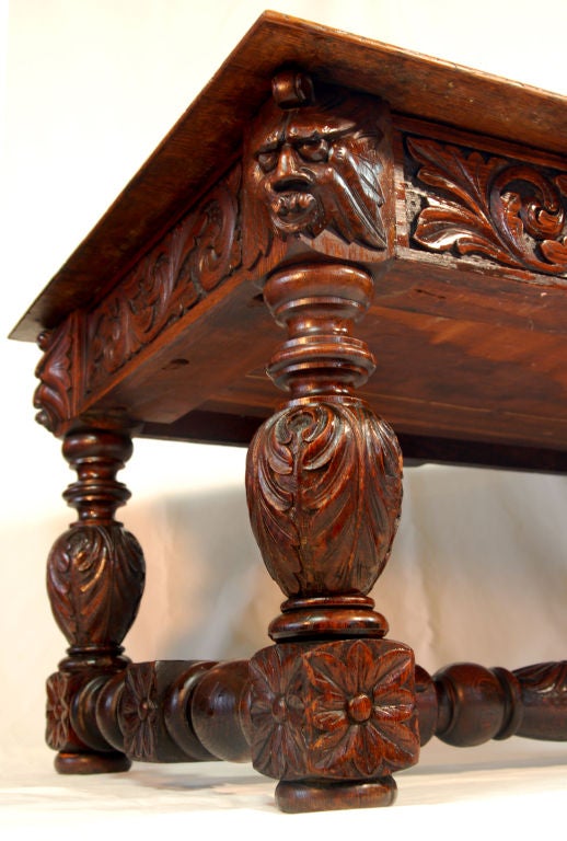 This intricately carved English oak Jacobian-style table features an inset leaf-carved border with several carved faces composed of foliage or 