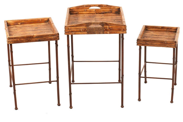 Late 20th century, Tommy Bahama style set of three nesting tables fit inside each other. Wrought iron bases, attached burnt bamboo tray tops.