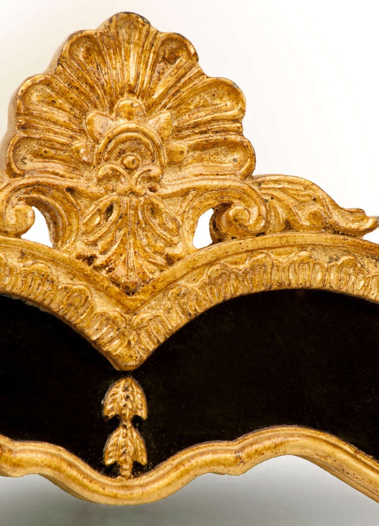 Miroir biseauté de style classique Queen Anne encadré, de belle forme, avec crête en forme de coquille, fleurs en cloche et sculptures feuillues. Laque noire et feuille d'or.
