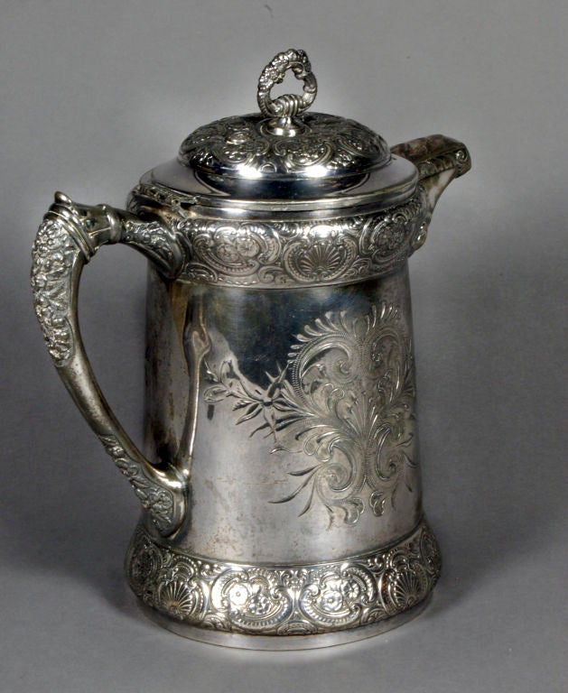 This unique silver pitcher by Barbour Brothers Silver Company of Hartford, Connecticut is overflowing with ornate detail. The pitcher has an overall hand-chased floral design with roses, and an embossed border with flowers, scrolls and scallops. It