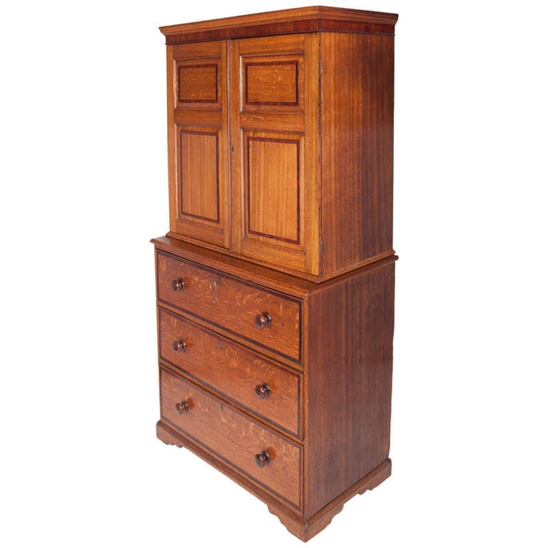 This two-piece secretary is constructed of oak with contrast mahogany banding, the compartmented fall front desk forms the top drawer of the base cabinet when closed, the upper cabinet has a pair of paneled doors with adjustable slide-out shelves