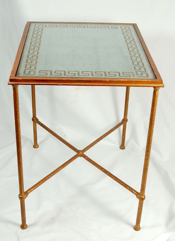 This reverse painted and silver plated glass top table features a fetching hand-painted Greek key border. The whole stands on a hammered bronze base with gold plating and X-shaped stretchers. This table was constructed in a wonderfully versatile