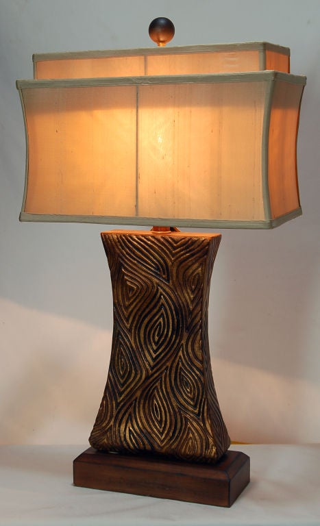 Cette magnifique lampe de table en résine est ornée d'un motif de labyrinthe tribal en or. Il repose sur une base en bois biseauté et comporte un embout sphérique en bois. La forme sensuelle en sablier du corps de cette lampe est accentuée par un