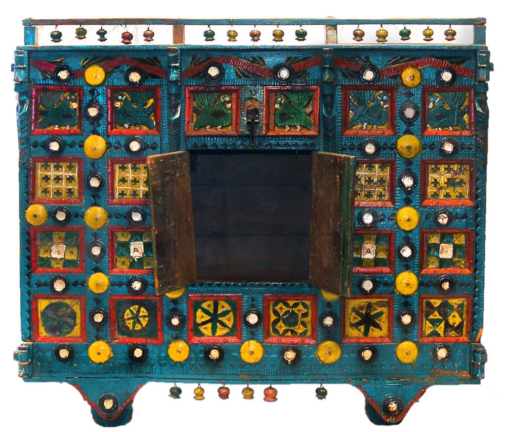 This antique Indian cart has been vividly painted with shades of cerulean blue, forest green, canary yellow, black and vermilion. The cart rolls on hand-carved wooden wheels. Hand-carved wooden bells painted in a rainbow of colors hang from both the