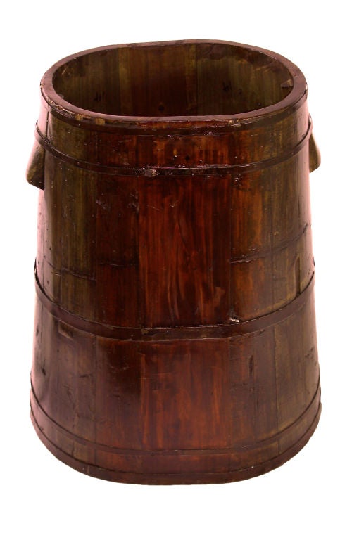 This handmade 20th century wooden grain barrel is built upon an oval base. The whole has an oblong shape which tapers toward the top.

To be strapped on the side of a water buffalo.