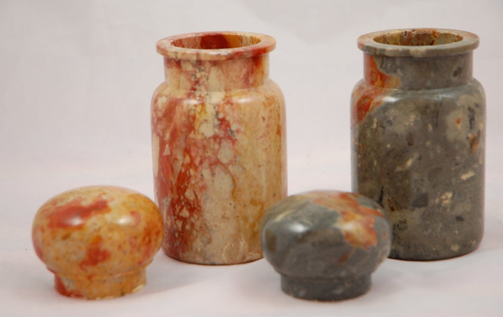 Cette noble paire de boîtes en marbre Pakastani Onyx présente un marbre magnifique et complexe dans les tons saumon, gris pierre et carmin. Ils sont fermés par des couvercles semblables à des boutons de porte. L'une des jarres présente une