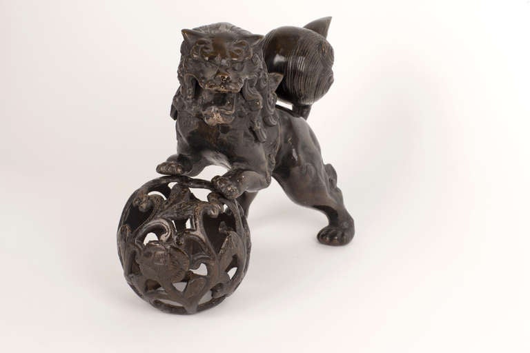 Cette pièce en fonte représente un lion gardien chinois statuaire (Foo Dog) qui tient fièrement en équilibre des deux mains une boule brodée, représentant la suprématie sur le monde. Une représentation traditionnelle et symboliquement puissante de