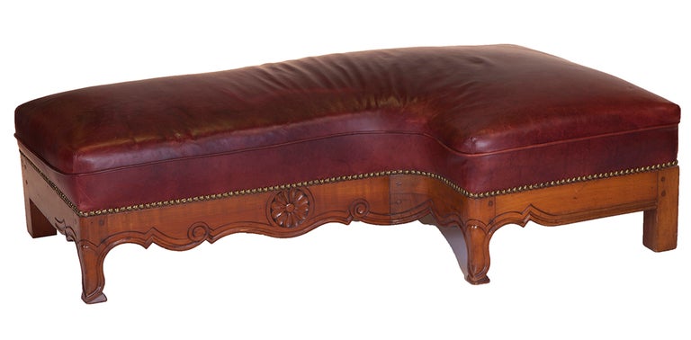 This red leather, carved French oak and nailhead trimmed hearthside bench has a curved interior for tending to the fire to seat in front of a fireplace.