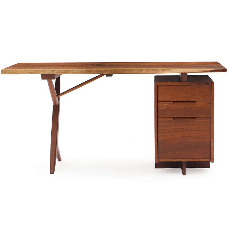 A superb example of an architectural cross-legged Conoid desk in walnut, having a floating, figured, single-slab live edge top and three (3) drawer pedestal with recessed pulls.