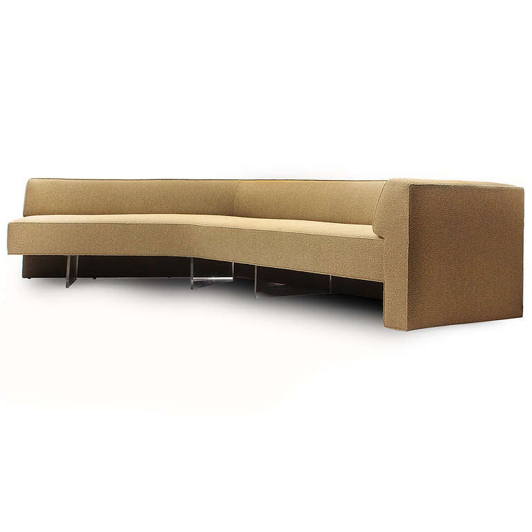 A dramatic, geometric and comfortable v-shaped sectional continuous-backed sofa of generous proportions, having an open end, lucite bases and finely upholstered in a cream bouclé fabric.
