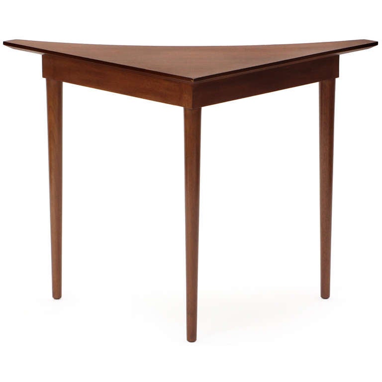 A corner table in walnut having three tapered dowel legs, with a triangulated apron and a geometric boomerang-form top.