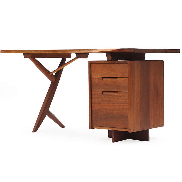 A superb example of an architectural cross-legged Conoid desk in walnut, having a floating, figured, single-slab live edge top and three (3) drawer pedestal with recessed pulls.