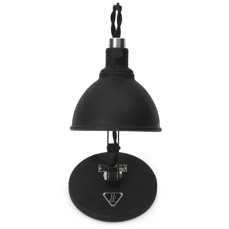 An industrial articulated adjustable task lamp in textured blackened steel, having a weighted disc base and a domed shade with a reflective mirrored interior.