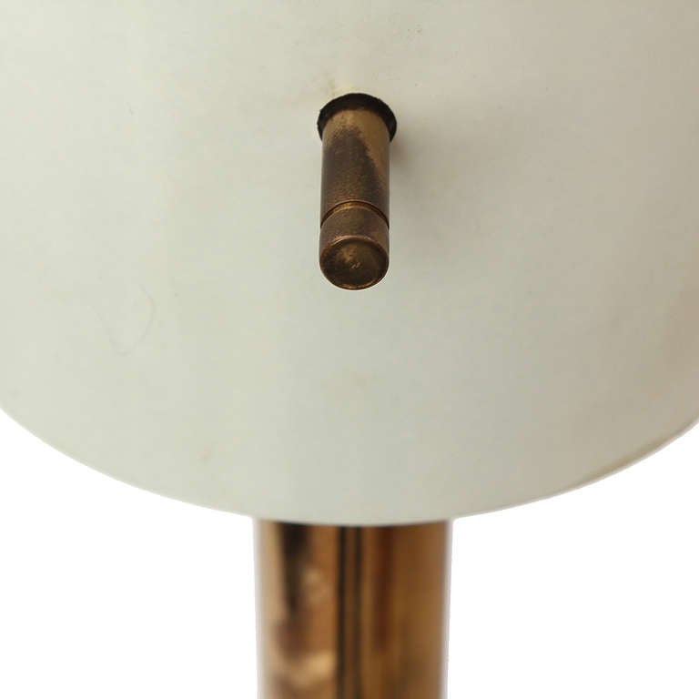 Une torchère élégante et minimaliste comportant une base et une tige en forme de disque en laiton et un abat-jour cylindrique laqué maintenu en place par des tiges filetées en laiton.