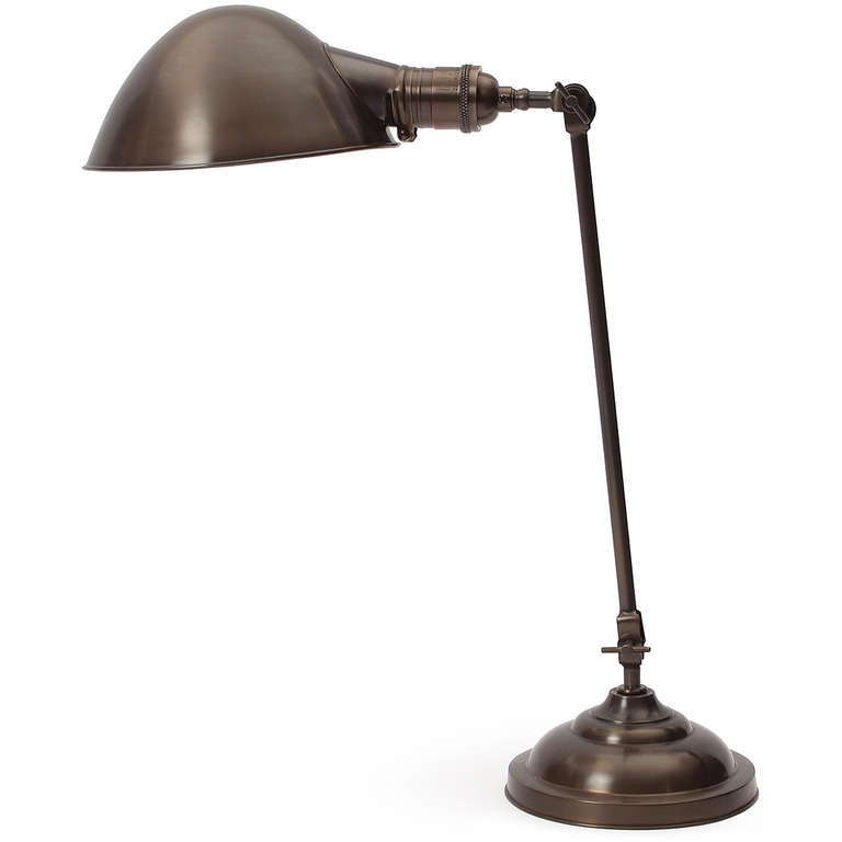 A highly adjustable and articulated industrial desk lamp in patinated brass having a stepped base, swiveling conical hood and exposed tension bars.
