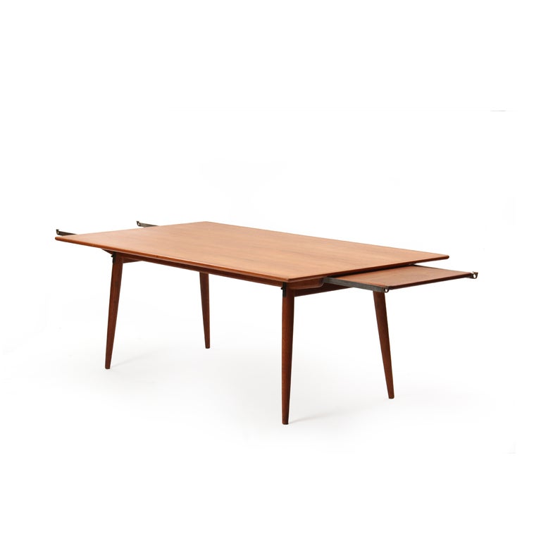 A rectangular dining table with a teak top concealing steel and brass pullouts and an innovative hidden leaf storage on a fumed oak base with splayed, tapered dowel legs. Two leaves are 17.5