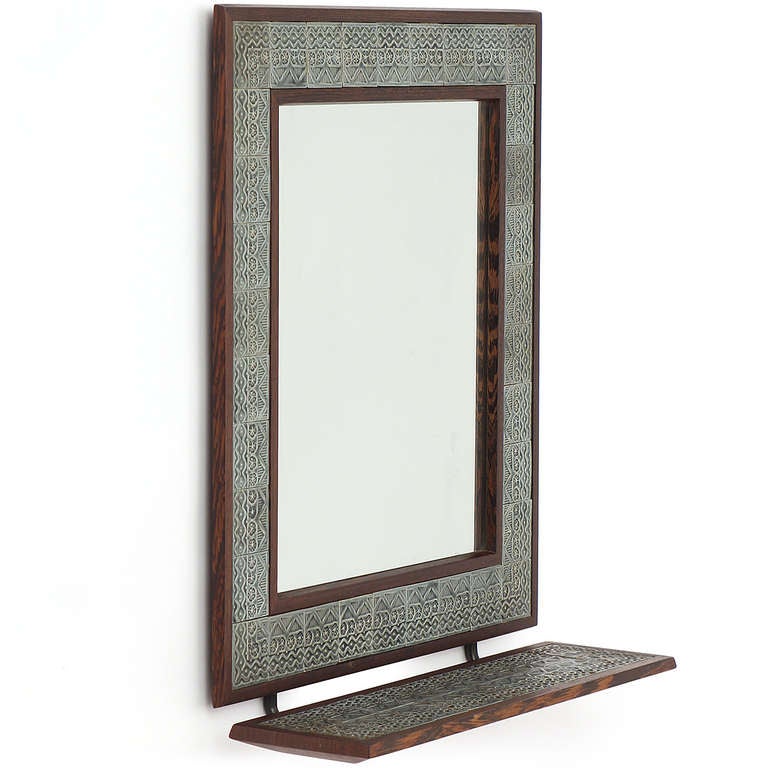 An impeccably crafted wenge-bordered wall mirror with attached matching shelf. The mirror and shelf are inlaid with patterned hand-crafted tiles.