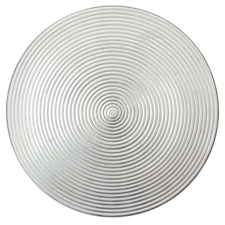 A sculptural pedestal occasional table in solid striated cast aluminum having a round disc top patterned with concentric rings.