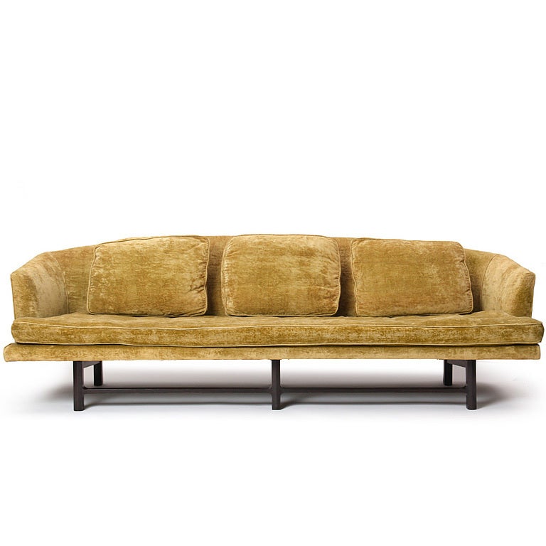 A large three seat sofa with an arched back on an dark walnut 6 leg base. This model was in production for a short period at Dunbar. Upholstered in gold velvet which requires re-upholstery. 
