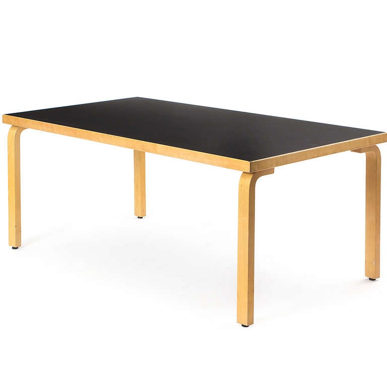 A sublimely simple desk or table having a rectangular top with a black laminate surface floating on four bentwood legs of Finnish birch.