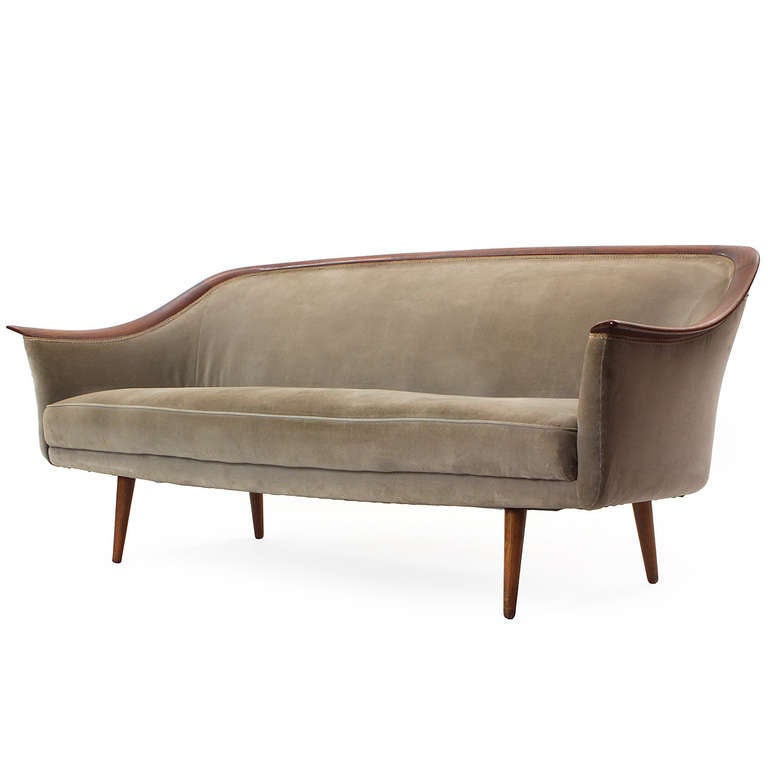 A sculptural and tailored continuous-arm upholstered sofa having a distinctive uninterrupted band of walnut defining both the arms and back, on turned walnut legs.