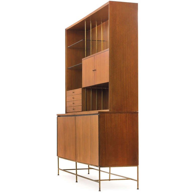 An elegant modernist etagere of rectilinear form in mahogany and brass having a lower cabinet with folding doors resting on square brass legs, supporting an upper cabinet with doors, glass shelves and drawers and open spaces.