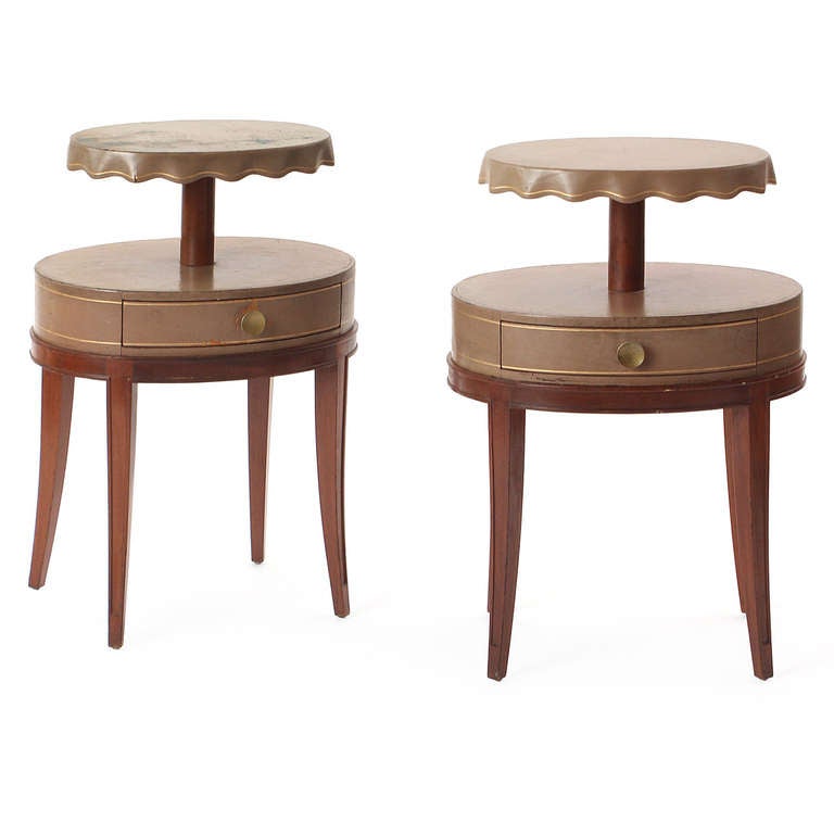 An elegant and unusual pair of two-tiered leather-wrapped side tables having single drawers, sculpted walnut legs and a raised oval platform with a scalloped edge.