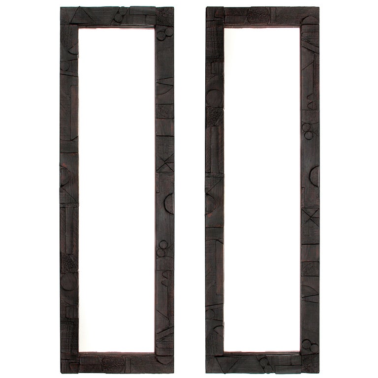 A pair of mirrors with an ebonized wooden frames with geometric carvings.