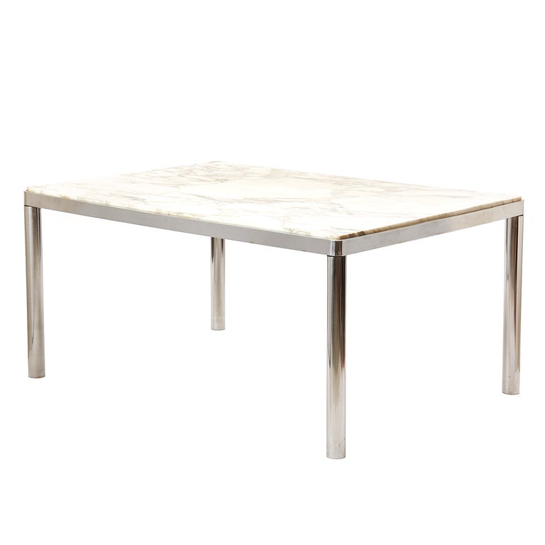 Ein rechteckiger Esstisch mit Edelstahlrahmen und einer weißen Marmorplatte. Zwei Tische können aneinandergereiht werden, um eine durchgehende 120