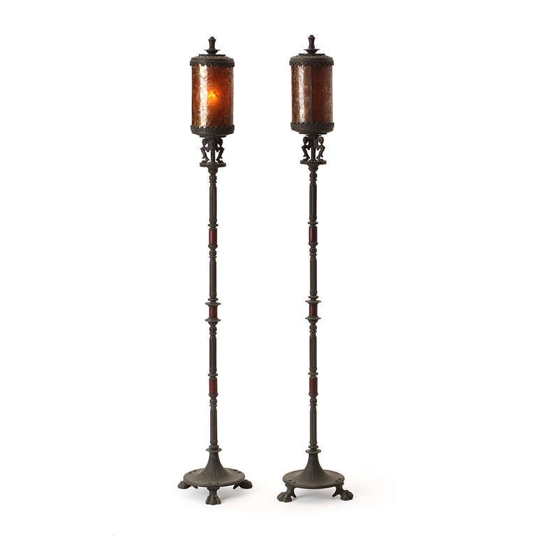 A pair of warmly patinated bronze torchiere lamps with intricate hand-forged details including stylized rams, hoofed feet and translucent shades made of amber-colored mica.