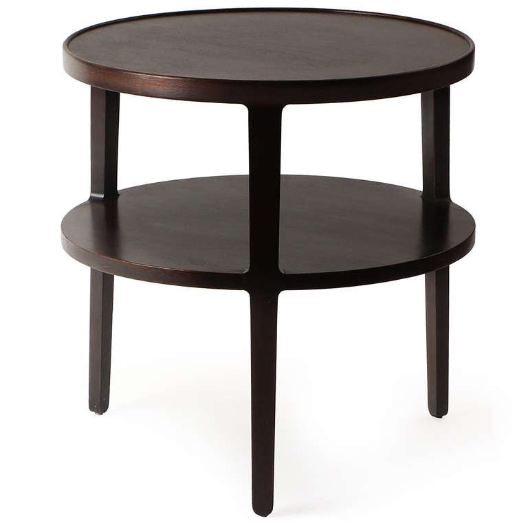 An early, circular, ebonized mahogany two-tier end table on three integrated tapered legs.