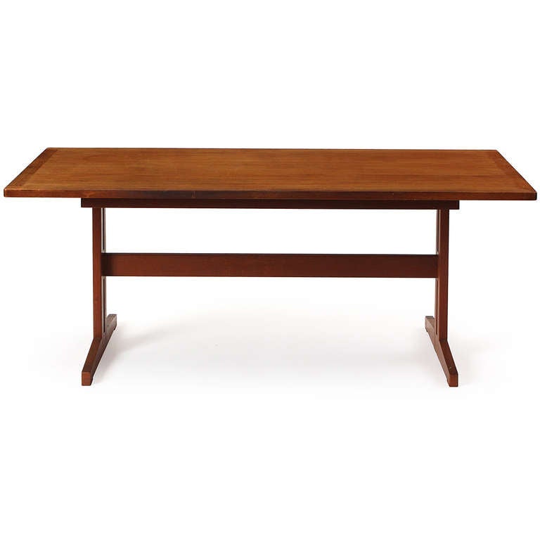 An elegant and simply detailed rectangular dining table crafted of teak and having a trestle base with a full length stretcher.