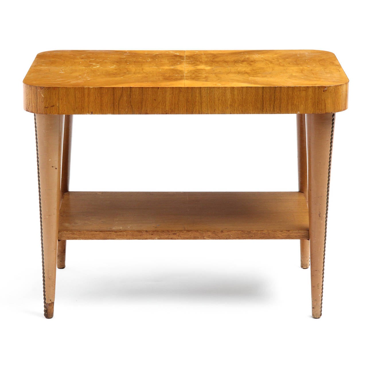 A Mid-Century Modern end table having a lower shelf and studded, tapering imitation leather-wrapped legs, the top surfaced with quadrants of bookmatched acacia burl. Designed by Gilbert Rohde. Made in USA by Herman Miller, circa 1940s.