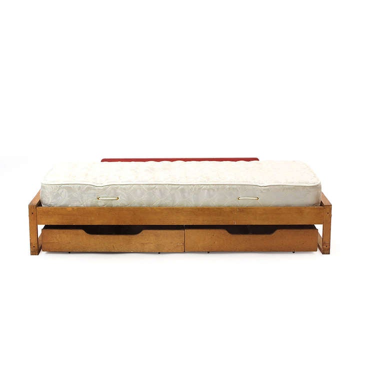 A superbly simple Finnish birch single bed with trundle like storage and a single red lacquered rail.