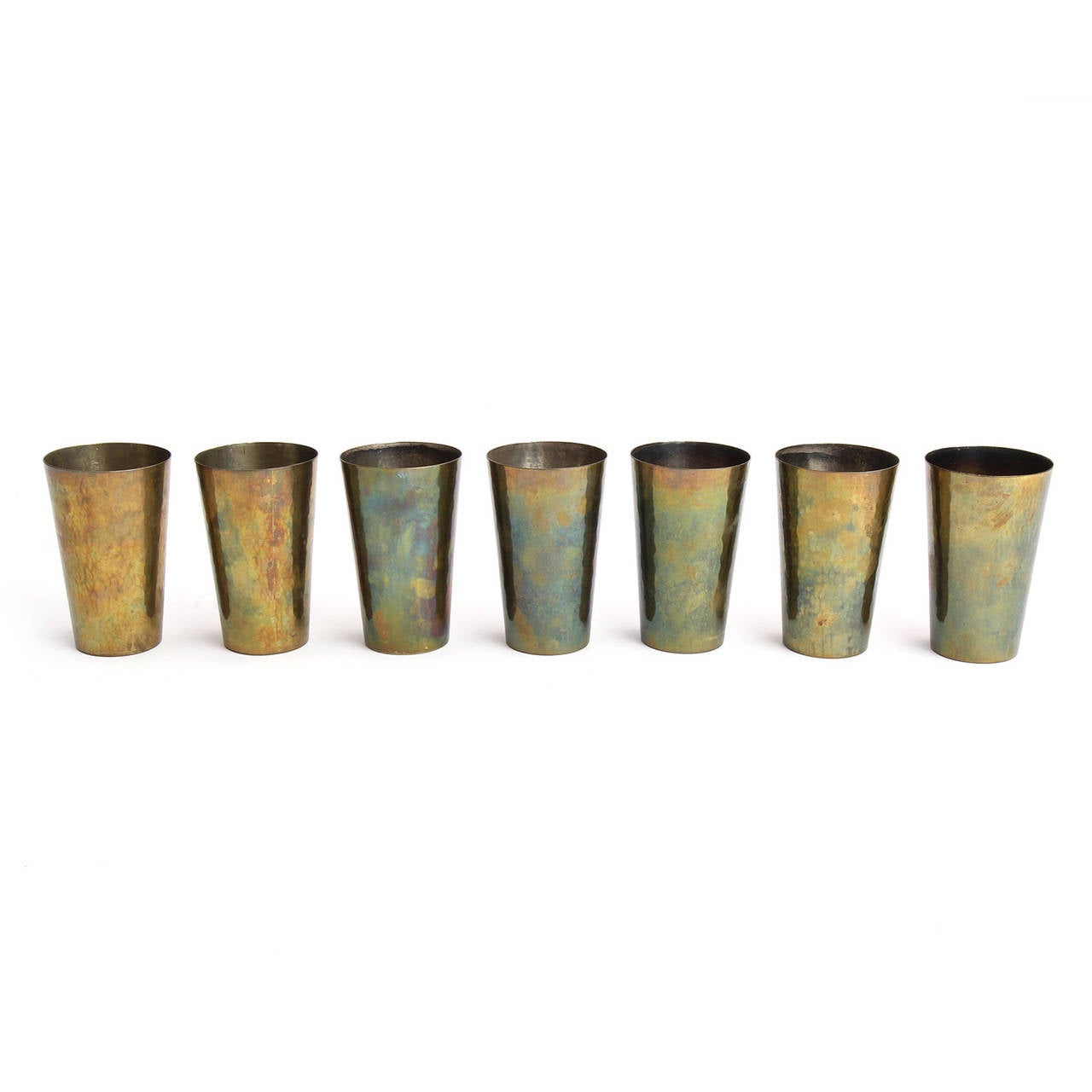 A fine and precisely rendered set of handmade hammered brass beakers or glasses having an elegant flaring form and a warm variegated patina.