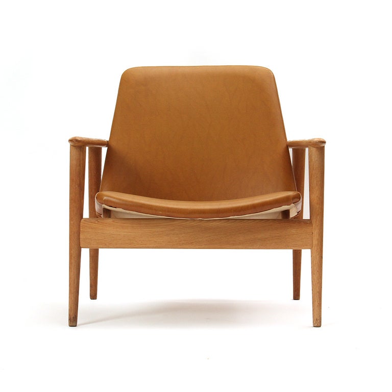 A pair of low lounge chairs with an oak frame and whiskey colored leatherette upholstery.