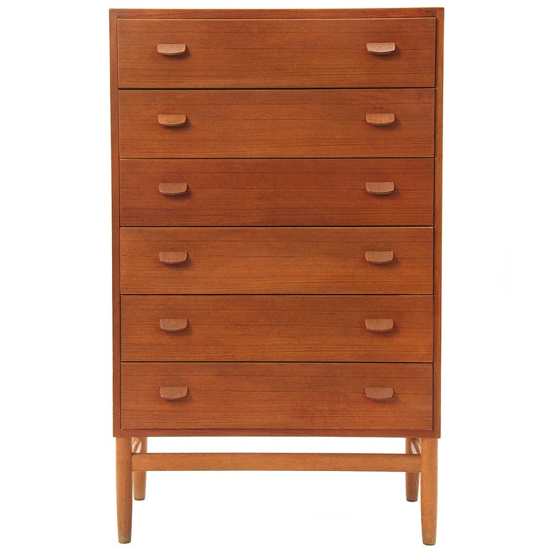 A spare and tall six (6) drawer teak dresser of rectilinear form having thin tab handles and floating on an architectural base.