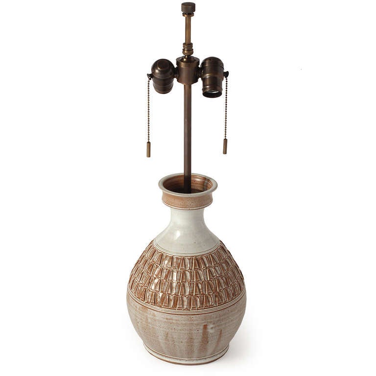 A hand-thrown ceramic table lamp having rhythmic and encircling embossed decoration and covered in a cream and mocha glaze.