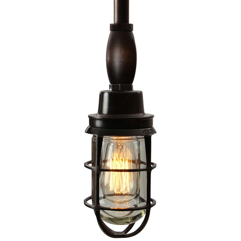 A finely rendered ceiling pendant crafted in patinated bronze that suspends from a rod and has a clear thick glass diffuser and an Edison bulb.