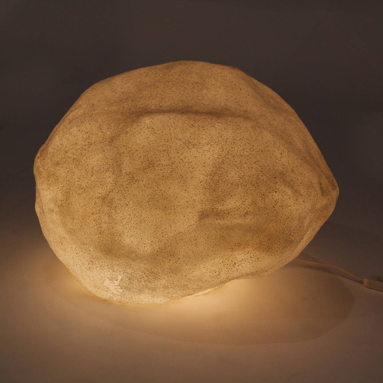 A group of naturalistic lamps having the form of natural stones, masterfully rendered in textured resin. The lamps emit a warm glow when lit.
