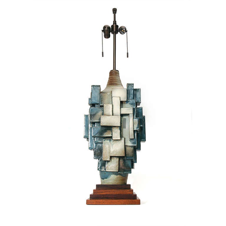 A ceramic table lamp on a stepped walnut base with a multi-faceted cubistic relief. White glaze with blue-grey accents.  25