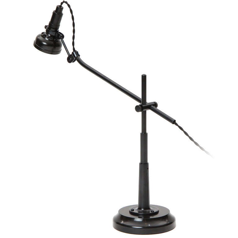An elegant table or desk lamp with a slender steel stem rising from a weighted base with a fully positionable secondary arm supporting a Bakelite shade.