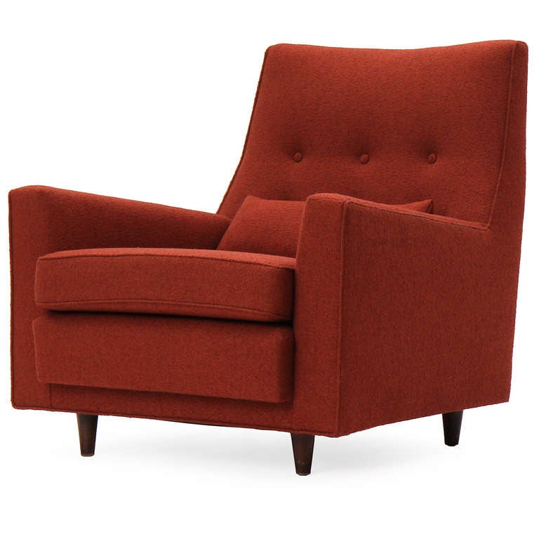 A pair of generously proportioned and sculptural upholstered button-tufted lounge chairs having upward-angled arms and turned walnut legs, upholstered in a rust-colored textured wool.