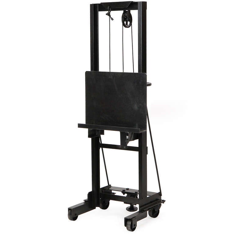 A heavy duty patinated steel industrial easel on casters having a cranking adjustment and exposed mechanisms. 
This easel can easily handle a heavy sculpture or a flat screen television.
Crank adjusts height of easel lip from 4.5